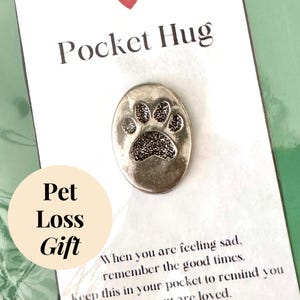 May include: A silver pocket hug with a paw print design. The card reads "Pocket Hug" and "When you are feeling sad, remember the good times. Keep this in your pocket to remind you are loved."