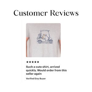 May include: A light gray t-shirt featuring a graphic illustration of a brown and white Corgi dog sitting in a golf cart with a golf bag in the back. The text Customer Reviews appears above the shirt, and a five-star rating is shown below it.