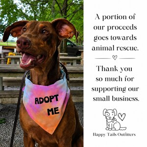 May include: A brown dog wearing a tie-dye bandana with the text ADOPT ME in black letters. The text on the right reads: A portion of our proceeds goes towards animal rescue. Thank you so much for supporting our small business. Happy Tails Outfitters.