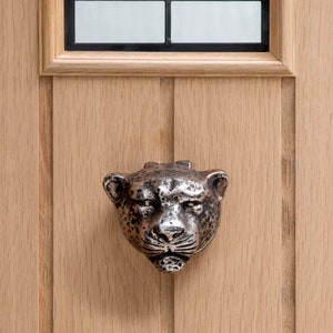 Peut inclure: Un heurtoir de porte en métal argenté en forme de tête de jaguar. Le heurtoir est monté sur une porte en bois.