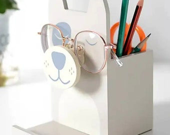 May include: A white wooden desk organiser shaped like a dog's head with a blue nose and eyes. The organiser has a slot for pens and pencils and a shelf for glasses.