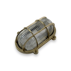 Op de afbeelding: Messing buitenwandlamp met een heldere glazen kap en een kooiconstructie. De lamp is ovaalvormig en heeft een gepolijste messing afwerking.