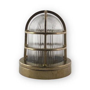 Op de afbeelding: Een messing lamp met een kooi en een heldere glazen kap. De lamp heeft een ronde voet en een kooi-achtig ontwerp rond de glazen kap.