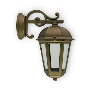 Op de afbeelding: Een gouden buitenwandlamp met een decoratief scrollontwerp en een heldere glazen kap.