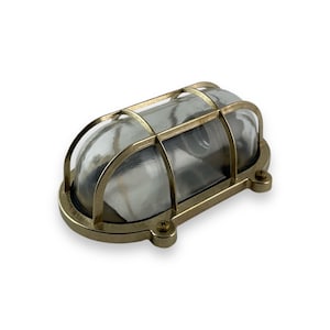 Op de afbeelding: Messing buitenwandlamp met een heldere glazen koepel en een kooi-achtig ontwerp. De lamp is ovaalvormig en heeft een traditionele stijl.