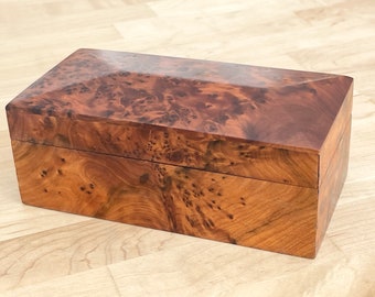 May include: A rectangular wooden box with a natural wood finish. The box has a lid and is made of a type of wood with a distinctive grain pattern.