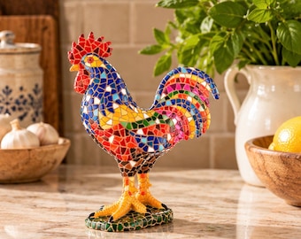 May include: A decorative rooster figurine crafted from colorful mosaic glass tiles. The bird features a vibrant mix of red, blue, yellow, and green shards, with a bright red comb and wattle, standing on a textured green mosaic base.