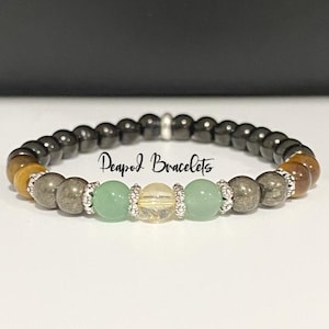 May include: A beaded bracelet featuring black hematite, tiger's eye, pyrite, green aventurine, and citrine beads. The bracelet has silver spacer beads and the text "Deapod Bracelets" is visible.