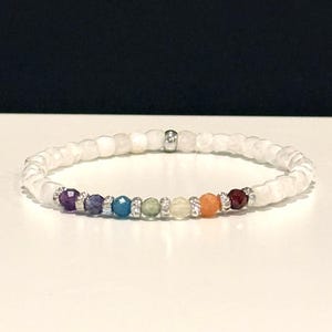 May include: A beaded stretch bracelet featuring small, faceted white moonstone beads. A central section displays seven colorful, faceted gemstone beads in purple, blue, teal, light green, yellow, orange, and red, separated by small silver-toned spacers.