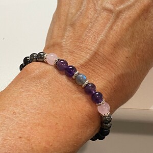 May include: A bracelet made with black hematite beads, amethyst beads, and rose quartz beads. The bracelet has silver accents.
