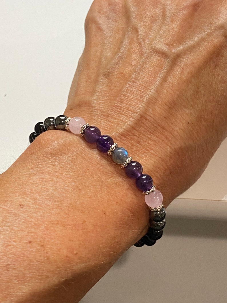 May include: A bracelet made with black hematite beads, amethyst beads, and rose quartz beads. The bracelet has silver accents.