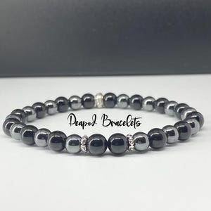 May include: A black and silver beaded bracelet with the text "Deapod Bracelets" on it.