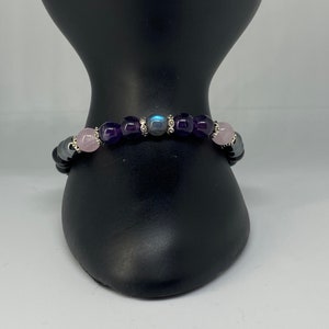 May include: A beaded bracelet with amethyst, rose quartz, and labradorite stones. The bracelet is on a black display stand.