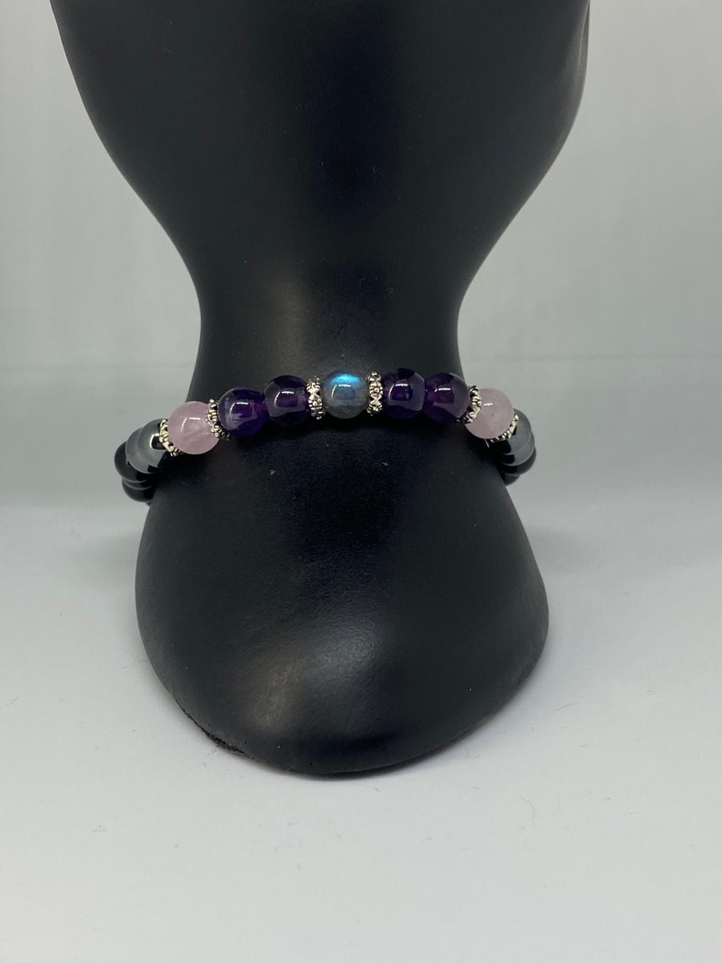 May include: A beaded bracelet with amethyst, rose quartz, and labradorite stones. The bracelet is on a black display stand.