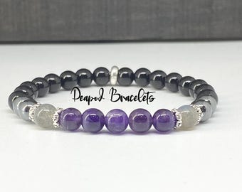 Puede incluir: Un brazalete hecho con cuentas de ónix negro, amatista y labradorita. El brazalete tiene un cierre plateado y está acentuado con cuentas plateadas.