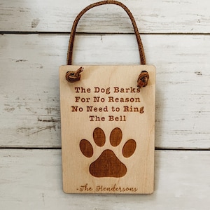 May include: A rectangular wooden sign with a leather loop for hanging. The sign features the text "The Dog Barks For No Reason No Need to Ring The Bell" and a paw print. The name "-The Hendersons" is below the paw print.