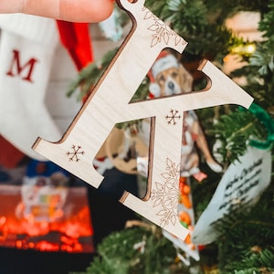 May include: A wooden Christmas ornament shaped like the letter K. The ornament is decorated with snowflakes and has a string for hanging.