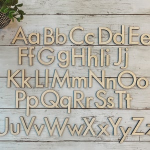 May include: Wooden alphabet letters in uppercase and lowercase, arranged in alphabetical order on a white wood background. The letters are all in a simple, sans-serif font.