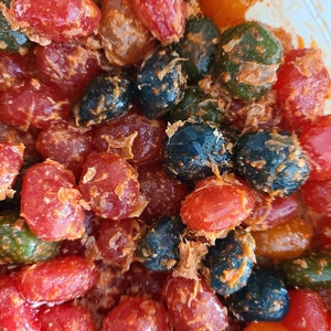 May include: A close-up of a bowl filled with colorful candy. The candy is a mix of red, orange, green, and black. The candy is coated in a white powder.