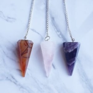 May include: Three crystal pendulums with silver chains. The pendulums are made of carnelian, rose quartz, and amethyst.