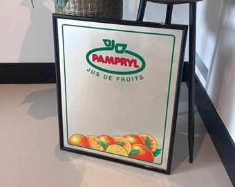 May include: A black framed mirror with a green and red logo that says "Pampryl Jus de Fruits". The logo is surrounded by a white oval. The mirror is reflecting a group of oranges.