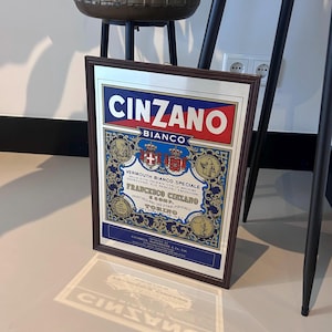Peut inclure: Ancienne affiche encadrée de Cinzano Bianco. L'œuvre présente le logo Cinzano en rouge et blanc, avec des détails bleus et dorés ornés. Le cadre est de couleur marron foncé.