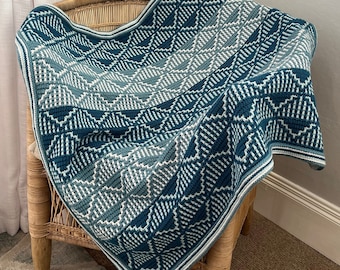 May include: A teal and white crocheted throw blanket with a geometric pattern. The blanket is draped over a wicker chair.