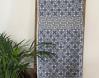 May include: A blue and white crocheted blanket with a geometric pattern is draped over a wooden ladder. The blanket features a repeating square design with a cream-colored border. A wicker basket with a green plant is in the foreground.