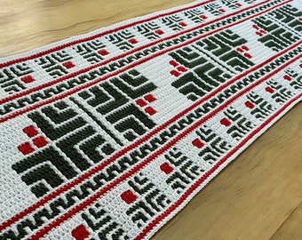 May include: A white crocheted table runner with a repeating geometric pattern in red and dark green. The runner features a central design with a border of red lines and geometric shapes. The runner is approximately 60 inches long.