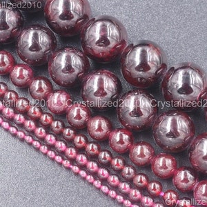May include: Assortment of red garnet gemstone beads in various sizes. The beads are round and smooth, with a polished finish. The beads are arranged in rows, with the largest beads at the top and the smallest beads at the bottom.