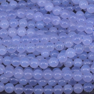 May include: A close-up image of a strand of light blue round beads. The beads are smooth and polished, and they are arranged in a random pattern.
