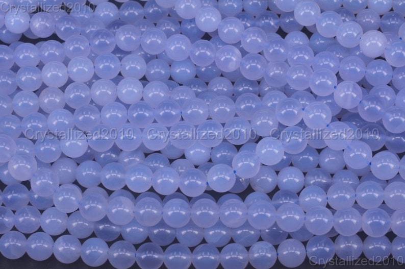 May include: A close-up image of a strand of light blue round beads. The beads are smooth and polished, and they are arranged in a random pattern.