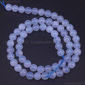 May include: A strand of light blue round gemstone beads. The beads are smooth and translucent, with a slight shimmer. The beads are strung on a thin blue thread.