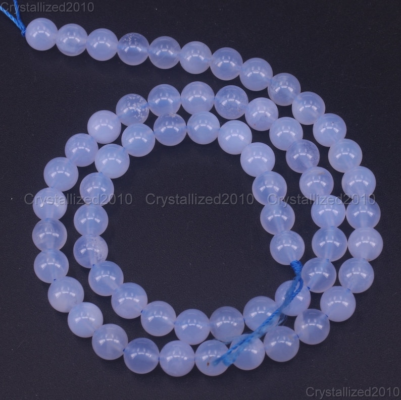 May include: A strand of light blue round gemstone beads. The beads are smooth and translucent, with a slight shimmer. The beads are strung on a thin blue thread.