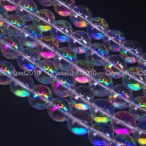 May include: Strands of clear, iridescent beads with a rainbow sheen. The beads are round and strung together, reflecting colours like pink, blue, and green. The beads are on a dark background.