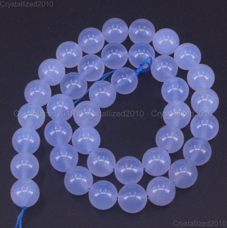 May include: A strand of light blue round gemstone beads. The beads are smooth and translucent, with a slight shimmer. The beads are strung on a blue thread.