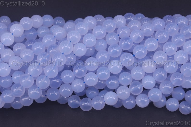 May include: A close-up of a strand of light blue round gemstone beads. The beads are smooth and polished, and they have a translucent appearance.