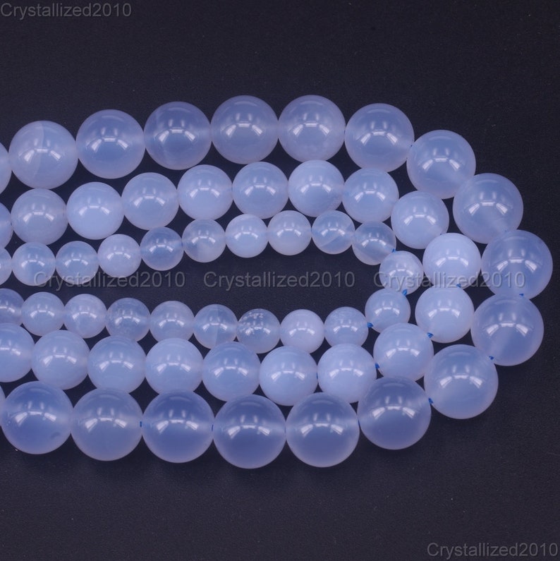 May include: A strand of light blue round gemstone beads. The beads are smooth and polished, and they have a translucent appearance.