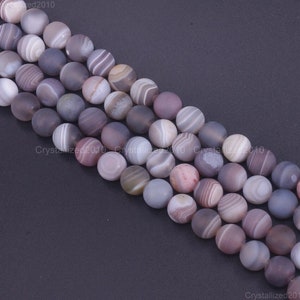 May include: Close-up of strands of round gemstone beads in various shades of grey, lavender, and white. The beads have a matte finish and a banded pattern. Each bead is approximately 8mm in diameter, suitable for jewellery making.