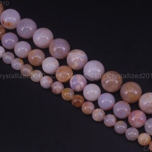 May include: Several strands of round gemstone beads in shades of purple, peach, and brown. The beads are different sizes and have a polished finish. They are strung together, ideal for crafting jewellery.