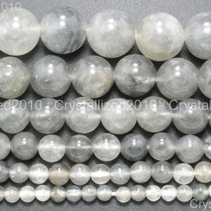 May include: A strand of round, translucent, gray and white beads. The beads are of varying sizes, with the largest beads being approximately 1 inch in diameter. The beads are arranged in rows, with the smallest beads at the bottom and the largest beads at the top.