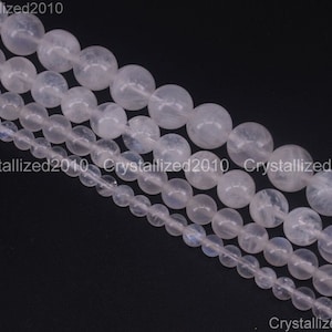May include: A strand of white moonstone beads in various sizes. The beads are round and smooth, with a translucent appearance. The beads are strung on a clear thread.