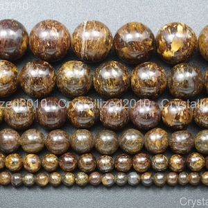Puede incluir: Una colección de cuentas redondas de piedra preciosa de varios tamaños, de color marrón y dorado. Las cuentas tienen un aspecto moteado y veteado.