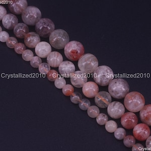 May include: A strand of round, translucent beads with red and orange inclusions. The beads are strung on a clear thread and are approximately 8mm in diameter.