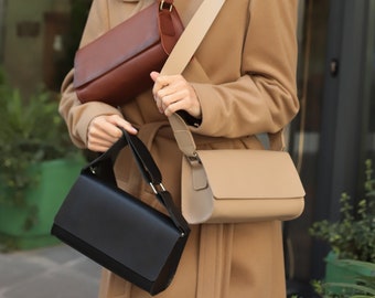 May include: A woman wearing a camel-colored coat carries three different handbags. The handbags are a brown crossbody bag, a beige crossbody bag, and a black satchel bag.