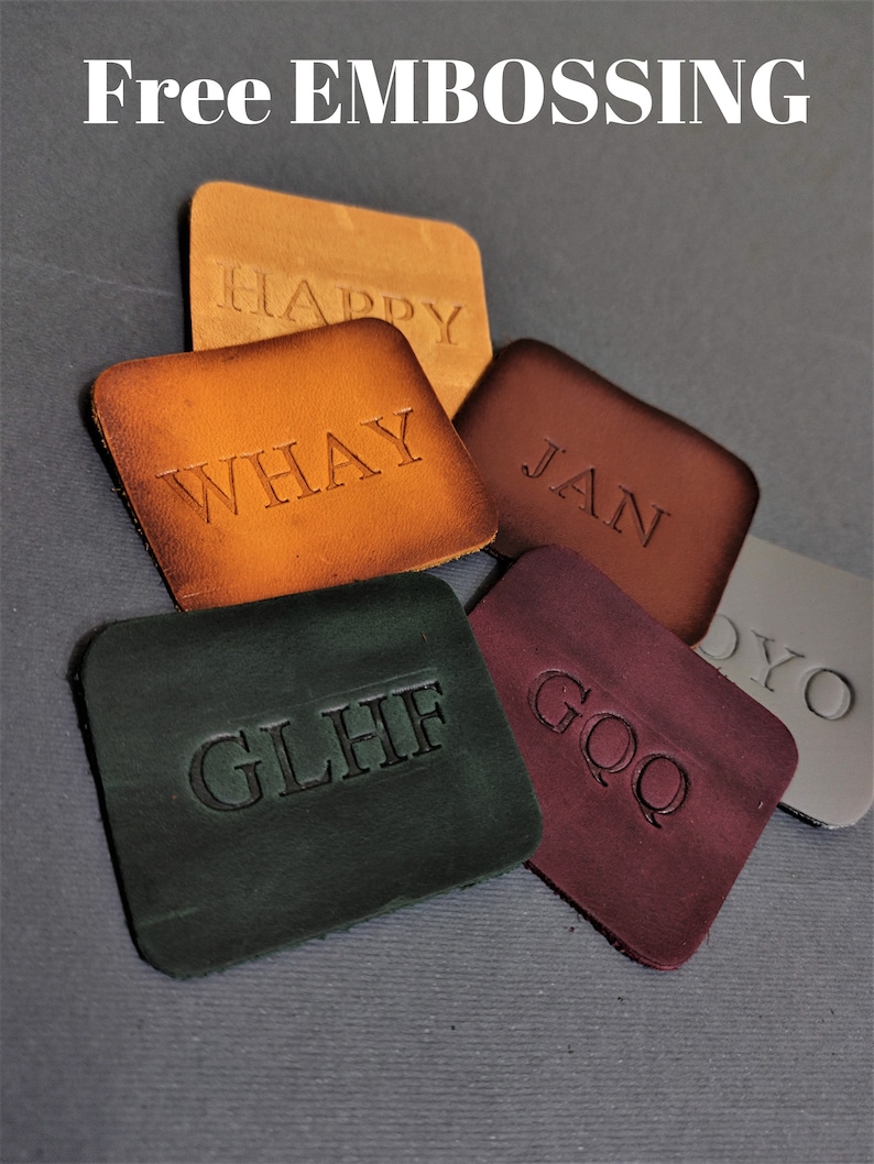 May include: Five leather patches with different names embossed on them. The names are "HAPPY", "WHAY", "JAN", "GLHIF", and "GOQ". The patches are arranged in a pile on a gray surface. Free embossing is offered.