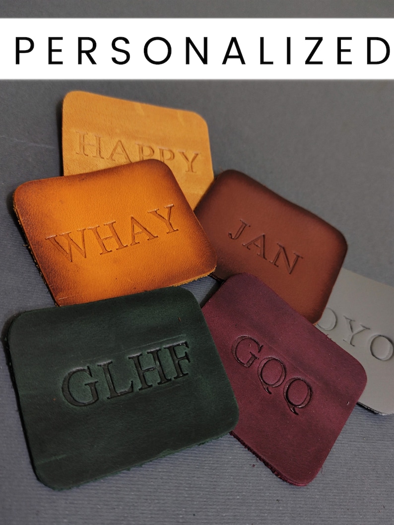 May include: Five leather patches with different colours and embossed text. The patches are brown, orange, maroon, green, and grey. The text on the patches reads "HAPPY", "WHAY", "JAN", "GLHF", and "GOQ".
