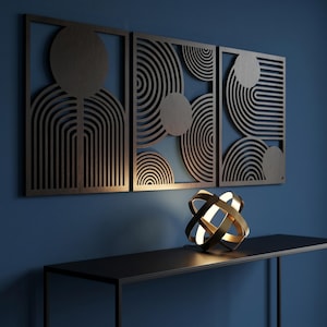 May include: Three rectangular dark brown wooden wall panels featuring intricate laser-cut geometric patterns of circles and parallel lines. A spherical gold metal lamp with intersecting rings sits on a black console table below the panels.