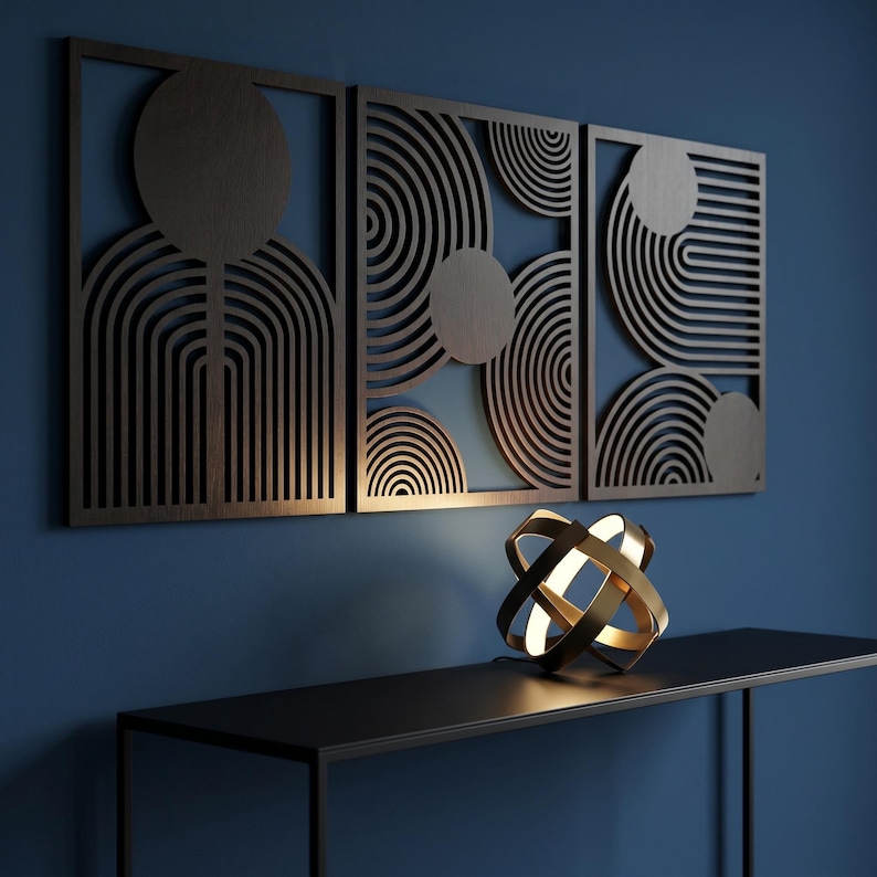 May include: Three rectangular dark brown wooden wall panels featuring intricate laser-cut geometric patterns of circles and parallel lines. A spherical gold metal lamp with intersecting rings sits on a black console table below the panels.