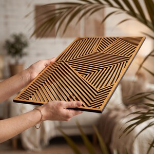 May include: A rectangular wooden wall art panel featuring a laser-cut geometric pattern of intersecting lines in light brown wood against a solid black background, creating a series of repeating angular shapes across the entire surface.